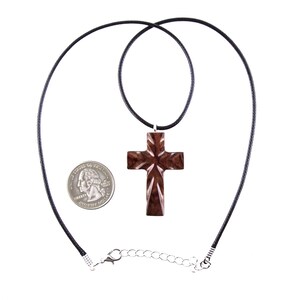 Dark brown wooden cross necklace with a black cord. The cross is intricately carved and has a slightly glossy finish.  A quarter is shown for scale, highlighting the pendant's size. The necklace features a simple clasp. This religious jewelry is perfect for everyday wear.