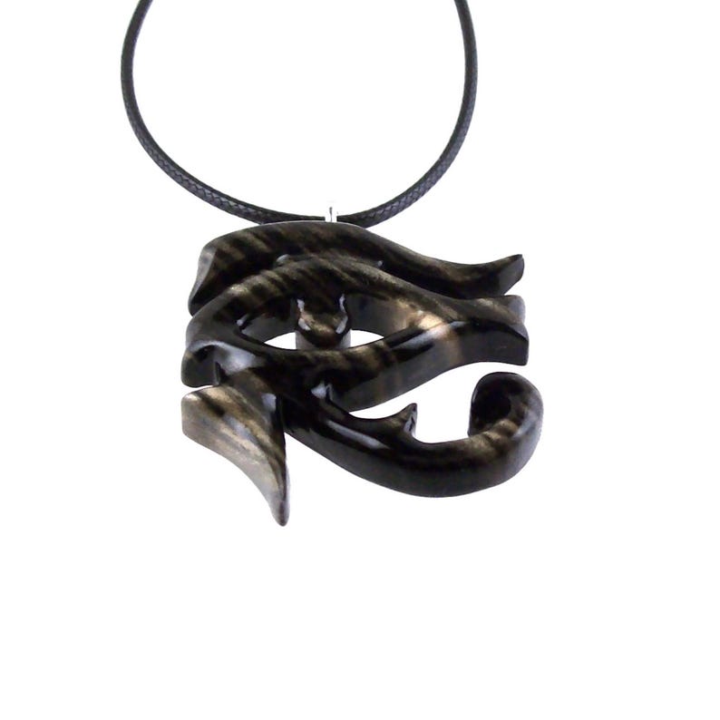 A wooden pendant necklace in black and brown, with a intricate design and a glossy finish. The pendant is shaped like an Eye of Horus and hangs from a black cord.