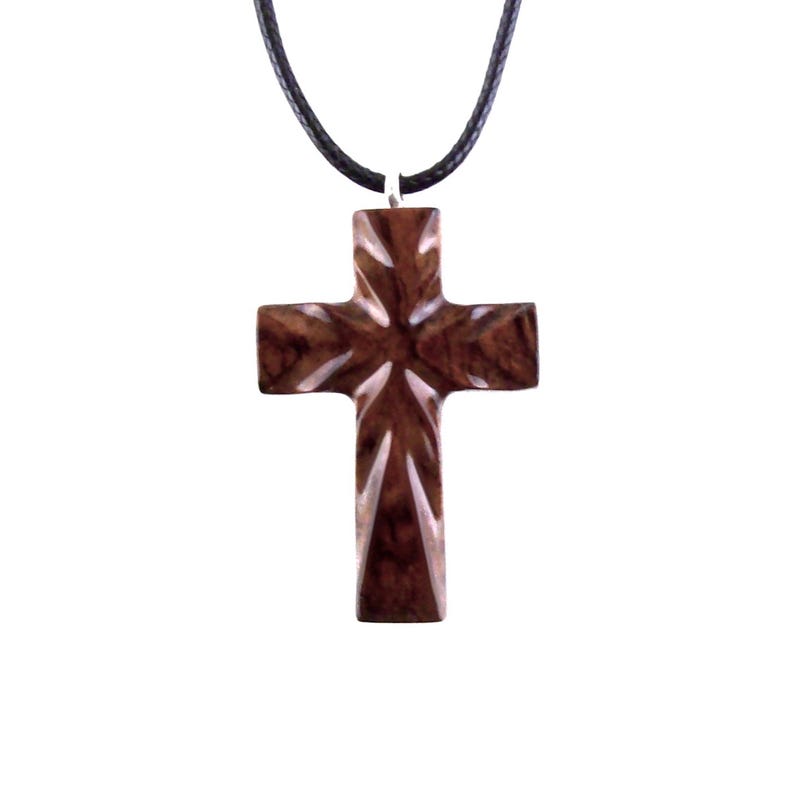 Dark brown wooden cross pendant necklace on a black cord. The cross features a detailed, carved design with a high-gloss finish.  The pendant is intricately carved with geometric patterns, creating a three-dimensional effect. The simple, elegant design makes it suitable for everyday wear or special occasions. This religious jewelry piece is a thoughtful gift for those seeking spiritual symbolism.
