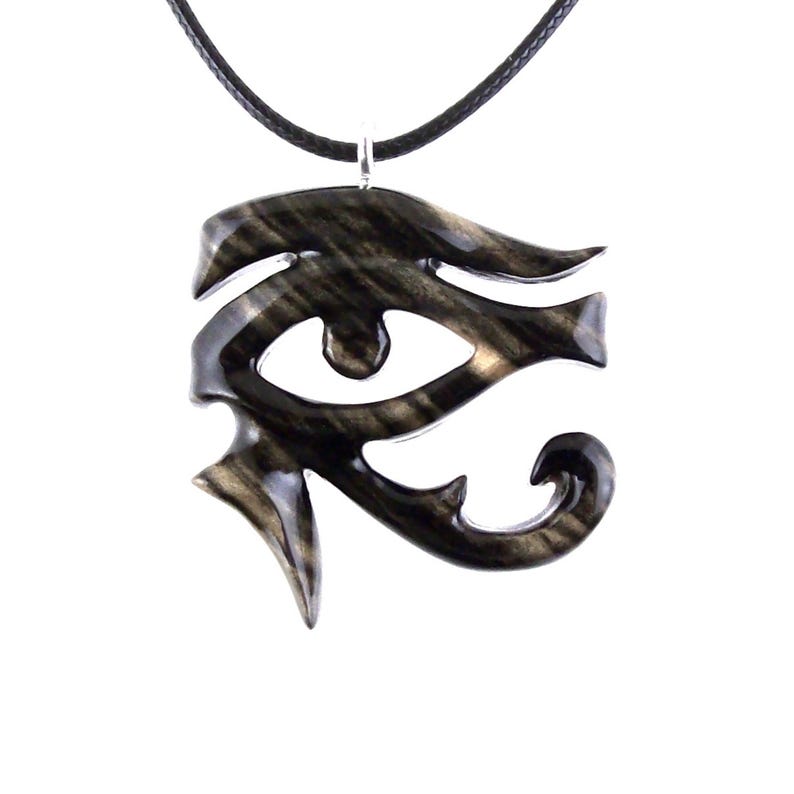 A wooden pendant in the shape of the Eye of Horus, a symbol of protection and good health in ancient Egyptian culture. The pendant is black with light brown streaks and is hanging from a black cord.