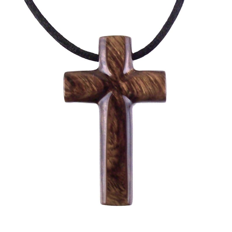 A dark brown wooden cross pendant necklace on a black cord. The cross has a carved, detailed design and a smooth, polished finish.  The wood grain is visible, adding to its rustic charm. This religious jewelry piece is perfect for everyday wear.