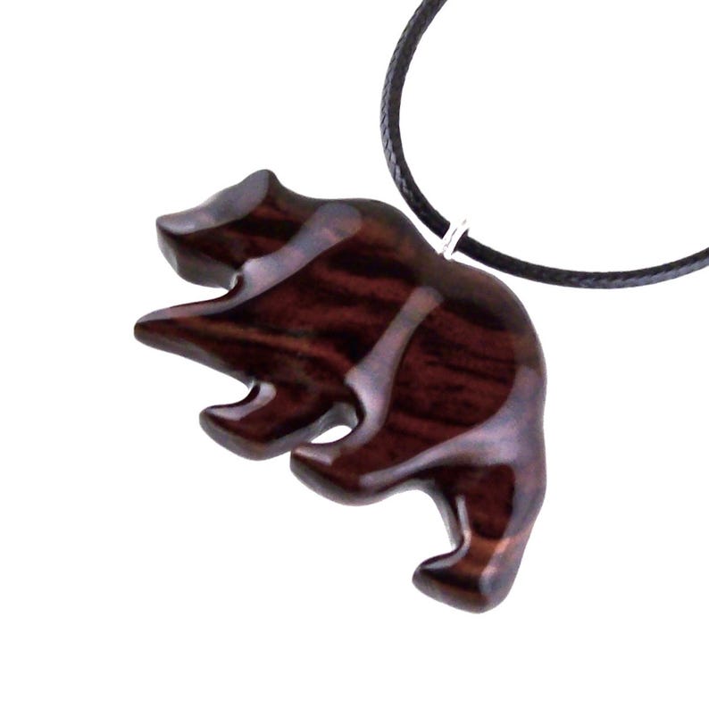 A wooden bear pendant with a dark reddish-brown finish and a black cord necklace. The bear is carved in a stylized form, with visible wood grain. The pendant is suspended from a black cord.
