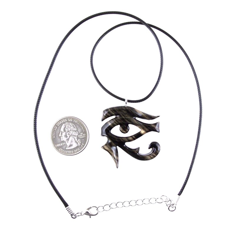 A wooden eye of Horus pendant necklace with a black cord. The necklace is made of wood and has a black and light brown color grain.