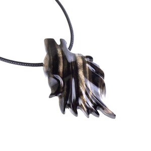 A black with brown streaks wooden wolf pendant necklace on a black cord. The pendant is intricately carved and has a detailed wolf head design.
