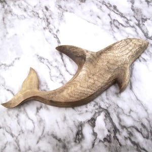 May include: A wooden carving of a dolphin, painted in shades of brown. The dolphin is leaping out of the water with its tail raised.