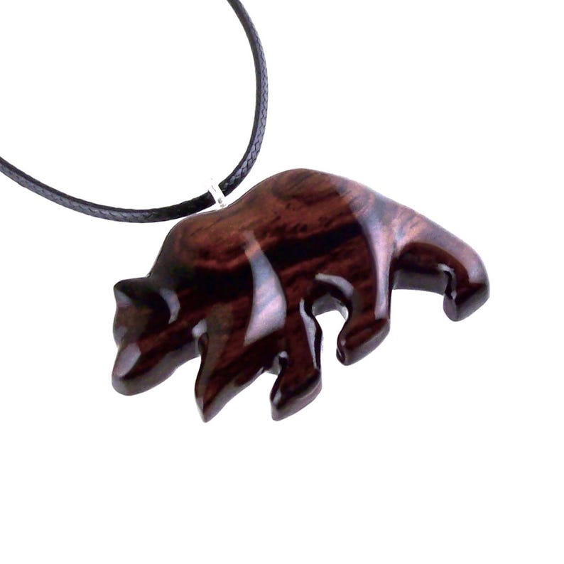 A reddish-brown wooden bear pendant on a black cord necklace. The bear pendant is carved with visible wood grain and has a glossy finish. The necklace is displayed against a white background.