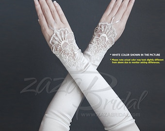 Puede incluir: Un par de guantes de satén blanco que llegan hasta el codo con delicados detalles de encaje y adornos de perlas. Los guantes están cruzados uno sobre otro, con el detalle de encaje visible en ambos guantes.