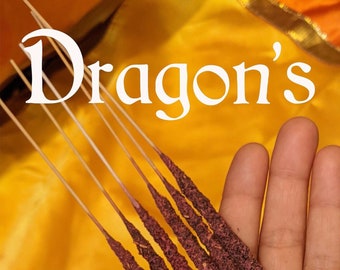 Può includere: Una mano tiene un mazzo di bastoncini di incenso al sangue di drago. I bastoncini sono di colore rosso scuro e hanno una consistenza ruvida. L'incenso è confezionato da Mango Mantras Divine Supplies.