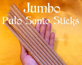 May include: A bundle of eight jumbo Palo Santo sticks, approximately 10 inches long, held in a hand. The sticks are a light brown color and have a rough texture. The text "Jumbo Palo Santo Sticks" is visible at the top of the image.