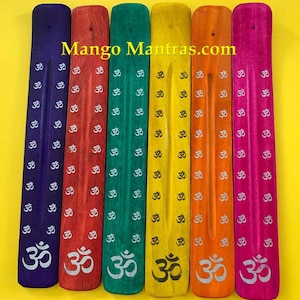 May include: Six wooden incense sticks with the Om symbol printed on them. The sticks are painted in different colors: purple, red, green, yellow, orange, and pink. The sticks are arranged in a row from left to right. The text "Mango Mantras.com" is printed on the top of the image.