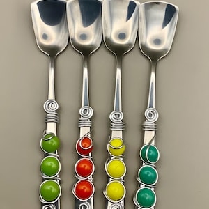 May include: Four silver-toned metal spoons with square-shaped bowls. Each handle is wrapped in silver wire and features three round beads in distinct colors: lime green, bright orange, lemon yellow, and teal green, arranged vertically.