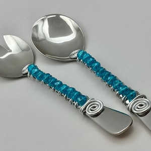 May include: A set of two stainless steel serving utensils with turquoise blue glass beads wrapped around the handles. The handles are wrapped with wire and have a spiral design at the end.
