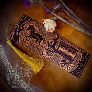 May include: A rectangular bookmark with a black carriage and horse design on an orange background. The bookmark has a gold tassel attached. The words "BAT IN YOUR BELFRY" are visible on the lower left corner.