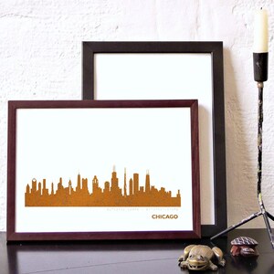 Könnte beinhalten: Ein gerahmter Druck der Skyline von Chicago in einem braunen Rahmen. Die Skyline ist eine Silhouette von Gebäuden in einem rostigen Orangeton. Der Druck ist auf weißem Hintergrund. Das Wort "CHICAGO" ist in Schwarz am unteren Rand des Drucks gedruckt.