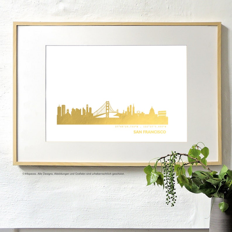 K&ouml;nnte beinhalten: Ein goldener Foliendruck der Skyline von San Francisco, einschlie&szlig;lich der Golden Gate Bridge, mit den Koordinaten und dem Namen der Stadt darunter.