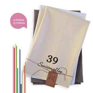 May include: A stack of three fabric swatches in beige, white, and grey. The top swatch has the number "39" and the word "Sonnenallee" printed on it. The bottom swatch has a small brown tag with the text "Made with Love" printed on it.