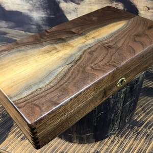 May include: A wooden box with a dark brown finish and a brass latch. The box is made of walnut wood and has a natural grain pattern.
