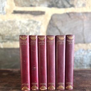 May include: A set of six vintage books from the American Statesmen series with deep red leather spines, gold-embossed lettering, and decorative floral motifs at the top and bottom of each spine. The titles include Andrew Jackson, Albert Gallatin, John Randolph, John Quincy Adams, Martin Van Buren, and Charles Francis Adams.