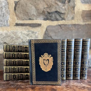 May include: A collection of antique books with dark blue covers and gold lettering. The books are titled "World Epochs" and feature decorative gold accents and a gold emblem on the front cover. The books are arranged on a wooden surface.