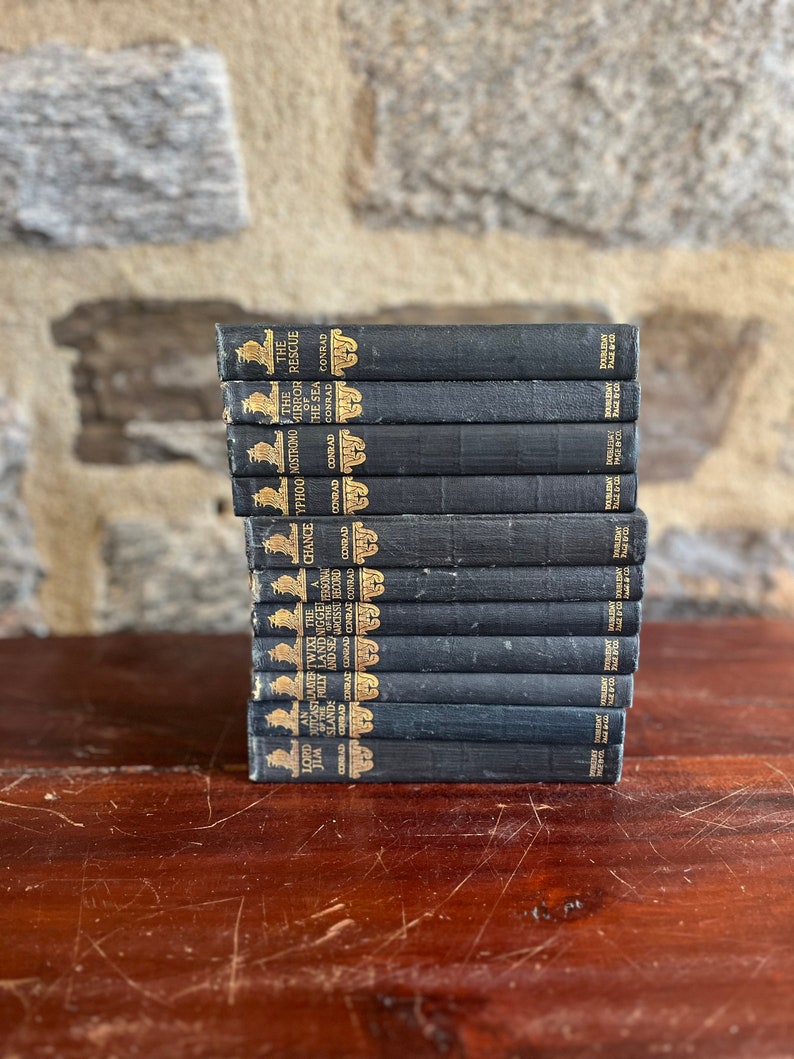 May include: A stack of 14 black hardcover books with gold lettering on the spines. The titles include "Lord Jim", "An Outcast of the Islands", "The Nigger of the Narcissus", "Typhoon", "Nostromo", "The Mirror of the Sea", and "The Rescue".