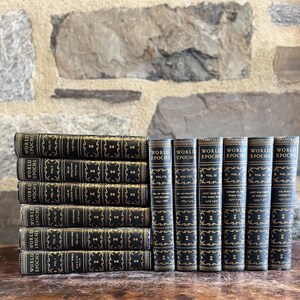 May include: A collection of antique books titled "World Epochs" with black covers and gold lettering. The books are stacked and arranged on a wooden surface against a stone wall background. The spines display volume numbers.