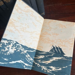 May include: An open book with a black cover and gold lettering. The book is open to a page with a black and white illustration of a ship sailing on a stormy sea.
