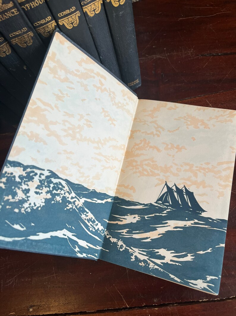 May include: An open book with a black cover and gold lettering. The book is open to a page with a black and white illustration of a ship sailing on a stormy sea.