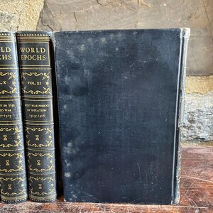 May include: A collection of antique books with black covers and gold lettering. The spines display the titles "WORLD EPOCHS" and "POST WAR PERIOD OF INFLATION". The books are arranged on a wooden surface, suggesting a vintage or historical theme.