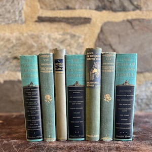 May include: A collection of vintage books with teal and gold covers, arranged in a row. The spines display titles like "The Virginians" and "Dance of the Quick and the Dead." The books are on a wooden surface.