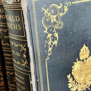 May include: Close-up of antique books with black covers and gold lettering and embellishments. The spines display titles like "World Epochs" and "The World Depression 1927-1936". The covers feature ornate gold designs.
