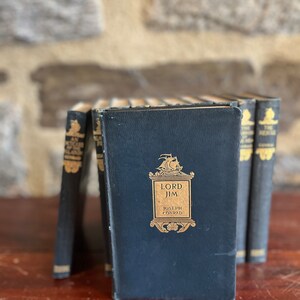 May include: A set of six vintage hardcover books with black covers and gold lettering. The title of the book in the center is "Lord Jim" by Joseph Conrad.