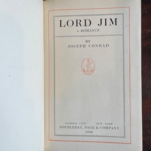 May include: A vintage book cover with the title "LORD JIM" in bold black font. The book is a romance by Joseph Conrad and was published by Doubleday, Page & Company in 1924.