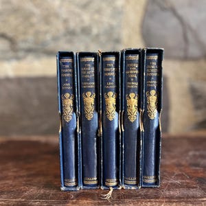 May include: A collection of five antique books with dark blue covers and gold lettering. The spines display titles like "The Pilgrim's Progress" and "The Kreutzer Sonata." The books are in a decorative box.