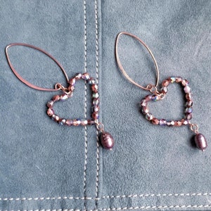 Może przedstawiać: Para kolczyków w kształcie serca ze złota różowego z iryzującymi koralikami kryształowymi i pojedynczym wisiorem z pereł na każdym kolczyku.