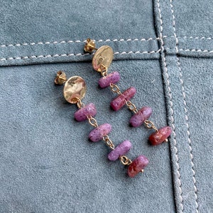 Puede incluir: Un par de pendientes de oro con un disco martillado y una cadena de cuentas de piedras preciosas rosas y moradas.