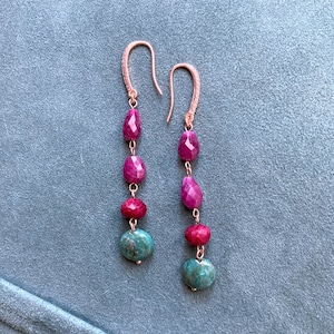 Peut inclure: Une paire de boucles d'oreilles pendantes avec des pierres précieuses roses et turquoise. Les boucles d'oreilles sont en or rose et ont un design délicat de chaîne.