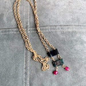 May include: A gold chain necklace with a green and black stone pendant and two pink stone accents.