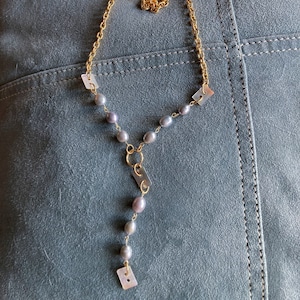 May include: A gold chain necklace with a Y-shaped pendant featuring a series of gray pearls and rectangular, iridescent shell accents.
