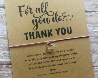 May include: A brown card with the text "For all you do... THANK YOU" printed in black. A pink string with a silver heart charm is tied around the card. The card also includes instructions for making a wish with the bracelet: "Close your eyes and make a wish, then tie this bracelet upon your wrist. When the bracelet breaks in two, the wish you made may just come true!" and the website address "www.3loveliesbowtique.etsy.com".
