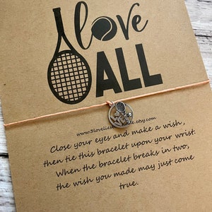 May include: A brown card with the text "I love ALL" in black lettering, a tennis racket and tennis ball graphic, and a silver charm bracelet with a tennis racket charm. The card also includes the text "Close your eyes and make a wish, then tie this bracelet upon your wrist. When the bracelet breaks in two, the wish you made may just come true."
