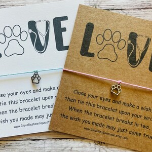 May include: Two cards with the word "LOVE" featuring a paw print and stethoscope design. Each card has a string bracelet with a paw charm. One card is white, the other is brown. Text on the cards reads "Close your eyes and make a wish..."