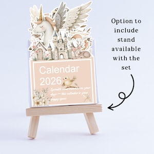 May include: A 2026 calendar with a whimsical design featuring a unicorn, castle, and deer. The calendar is displayed on a small wooden easel. The text on the calendar reads "Calendar 2026" and "Sprinkle some sunshine on your days - this calendar is your happy space."