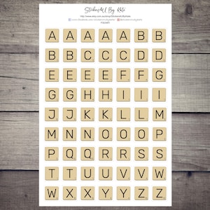 May include: A sheet of alphabet stickers featuring the letters A through Z in a Scrabble tile style. The stickers are printed on white paper with a beige background.