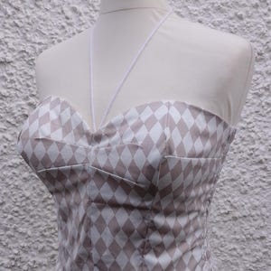 May include: A white and beige diamond patterned corset with white straps.