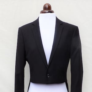 Peut inclure: Un tailcoat noir avec une fermeture à un bouton. Le tailcoat a un devant court et de longues queues à l'arrière.