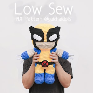 May include: A crocheted plush toy of Wolverine from the X-Men, holding a red X on his chest. The toy is yellow, blue, and black. The image text reads "Low Sew PDF Pattern @guichaidolls".