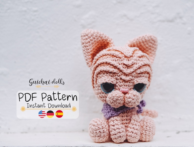 May include: A crocheted pink cat amigurumi with blue eyes and a purple scarf. The cat is sitting on a white surface. The image includes the text "Guichai dolls PDF Pattern Instant Download" with the flags of the United States, Germany, and Spain.