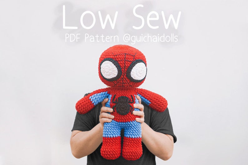 K&ouml;nnte beinhalten: Eine Person h&auml;lt eine rote und blaue geh&auml;kelte Spiderman-Puppe. Die Puppe hat ein schwarzes Spinnen-Symbol auf der Brust. Der Text "Low Sew PDF Pattern @guichaidolls" befindet sich &uuml;ber der Puppe.