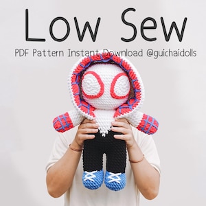 Może przedstawiać: Ręcznie robiona szydełkowa lalka w kostiumie superbohatera. Lalka ma białe ciało z czerwoną i niebieską bluzą z kapturem, czarne spodnie i niebieskie buty. Tekst "Low Sew" i inny tekst znajdują się u góry.