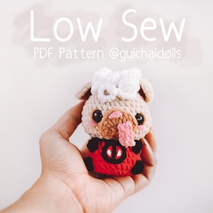 May include: A crocheted amigurumi toy of a pug wearing a red ladybug costume. The toy has a white crocheted flower on its head. The toy is being held in a person's hand. The text "Low Sew PDF Pattern @guichaidolls" is visible in the image.